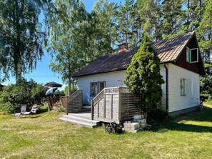 Une petite maison de plain-pied, dotée d’un toit en pente, d’une terrasse en bois et d’une cour clôturée.