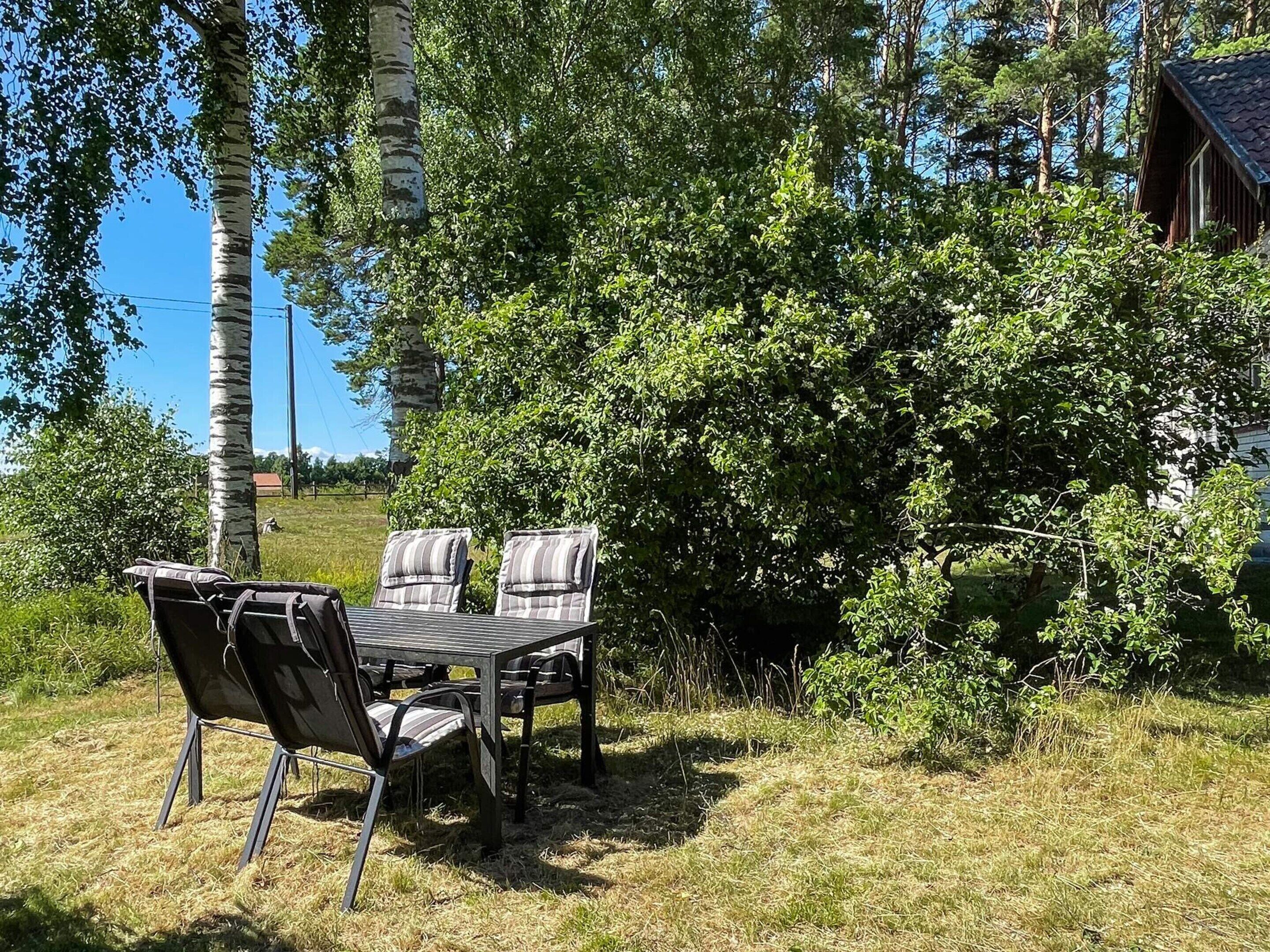 Ulkona oleva oleskelualue, jossa on pöytä ja tuoleja, ja jota ympäröi tiheä kasvillisuus ja avoin taivas.