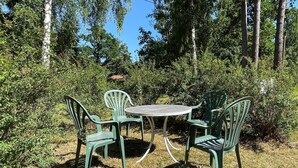 An outdoor seating area with a round table and four chairs, surrounded by dense greenery and trees. - 6 Person Holiday Home in Byxelkrok (Byxelkrok)