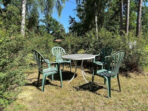 An outdoor seating area with a round table and four chairs, surrounded by dense greenery and trees. - 6 Person Holiday Home in Byxelkrok (Byxelkrok)