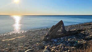 A rocky beach with a log in the foreground and the sun setting over the water. - 6 Person Holiday Home in Byxelkrok (Byxelkrok)