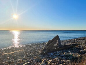 A rocky beach with a log in the foreground and the sun setting over the water. - 6 Person Holiday Home in Byxelkrok (Byxelkrok)