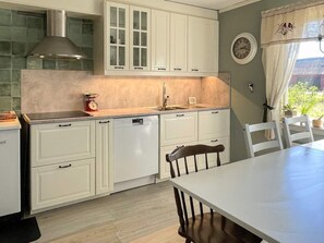 Une cuisine avec des meubles blancs, un four encastré et un coin repas comprenant une table et des chaises.