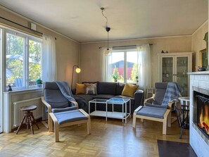Un salon comprenant un canapé, deux fauteuils, une table basse, une cheminée et une vue sur l’extérieur grâce à de grandes fenêtres.
