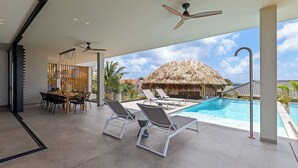 A modern outdoor pool area with lounge chairs, a dining table, and a ceiling fan. - Villa Quatrosol - an exclusive private resort under the sun! (Jan Thiel)