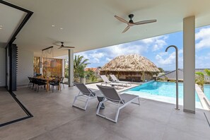 A modern outdoor pool area with lounge chairs, a dining table, and a ceiling fan. - Villa Quatrosol - an exclusive private resort under the sun! (Jan Thiel)