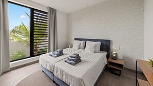 A modern hotel room with a large bed, a ceiling fan, a view of palm trees, and a geometric wall pattern. - Villa Quatrosol - an exclusive private resort under the sun! (Jan Thiel)