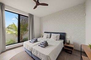A modern hotel room with a large bed, a ceiling fan, a view of palm trees, and a geometric wall pattern. - Villa Quatrosol - an exclusive private resort under the sun! (Jan Thiel)