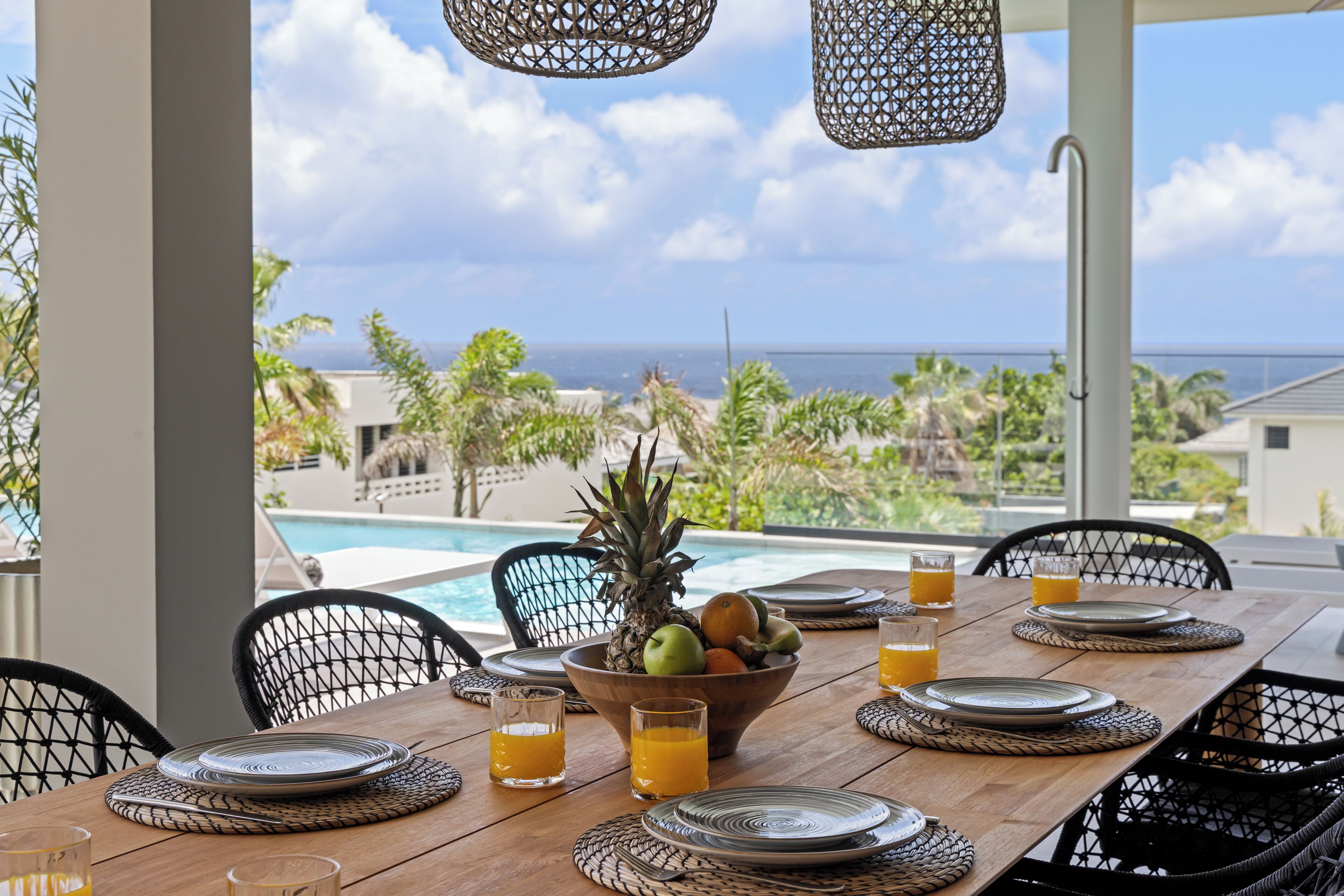 A dining table set for breakfast with a view of the ocean and pool.