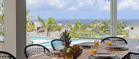 A dining table set for breakfast with a view of the ocean and pool.