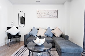 A modern living room with a grey sectional sofa, a black chair, a round glass coffee table, and a framed artwork on the wall.