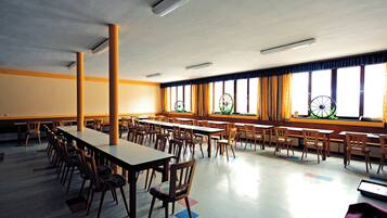 A large room with multiple tables and chairs, a high ceiling, and large windows with curtains.
