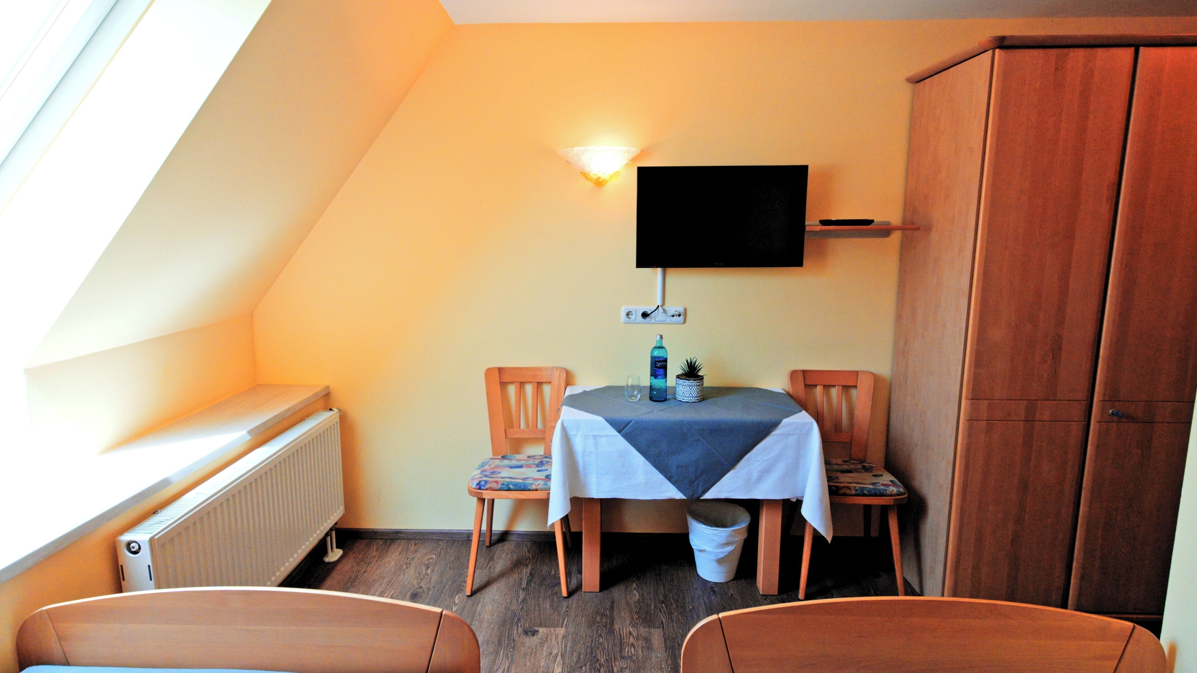 Ein kleiner Essbereich mit Tisch, Stühlen, einem an der Wand befestigten Fernseher und einer Heizung.
