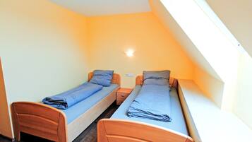 Un alojamiento pequeño de una sola habitación con dos camas individuales, una mesita de noche y una lámpara fijada a la pared.