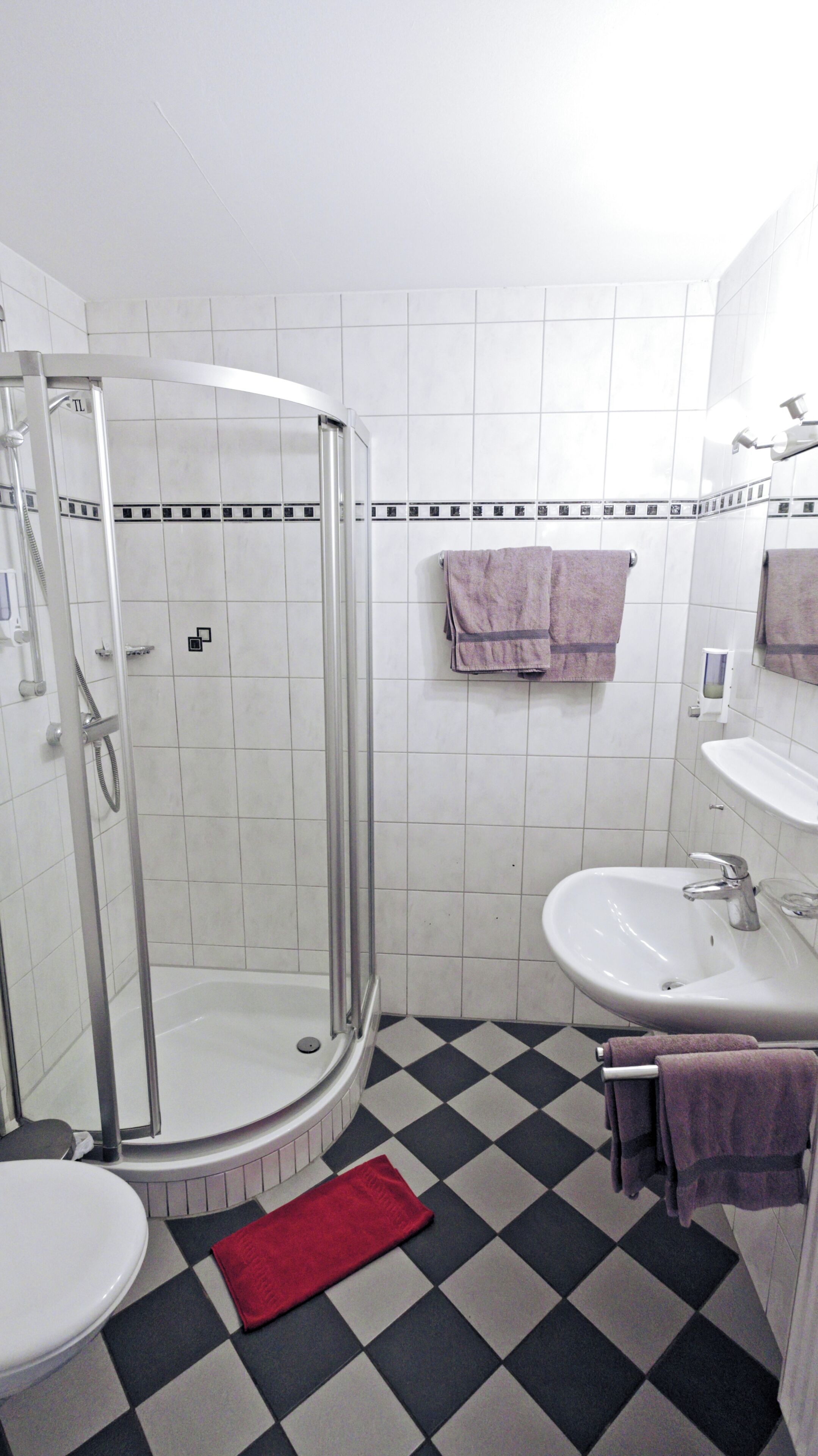 Un baño con ducha, inodoro, lavamanos y pisos de baldosas de cuadros.