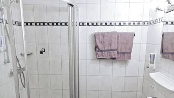 Un baño con ducha, inodoro, lavamanos y pisos de baldosas de cuadros.