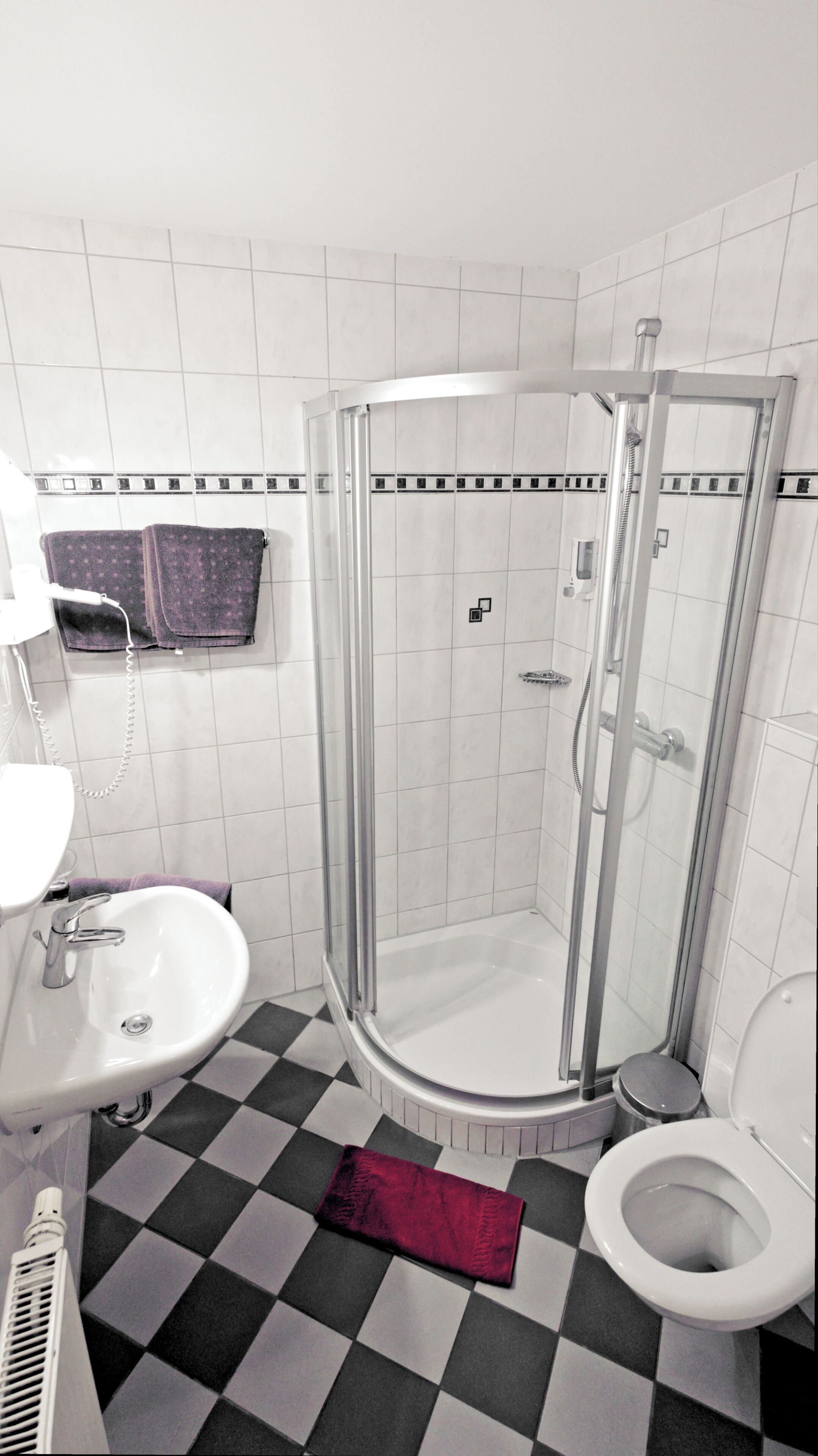 Un baño con ducha, inodoro, lavabo y suelo de cuadros.
