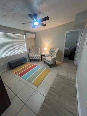 A room with a ceiling fan, two patterned armchairs, a bench, a striped rug, and a bed in the adjacent room. - Charming 3-bedroom house in serene Mims (Mims)