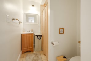 Un baño con un mueble de madera, cortina de ducha, inodoro y una lámpara fijada a la pared.