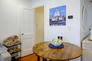 Una habitación con una mesa redonda de madera, un tazón de artículos de aseo, una puerta y un cuadro colgado en la pared de un edificio.