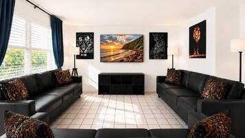 A modern living room with two black leather sofas, a large painting of a sunset, and a fireplace.