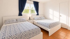 Ein Hotelzimmer mit zwei Betten, einem Deckenventilator, einem Fenster mit Vorhängen und einer Tür.