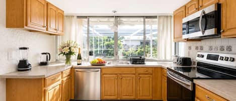 Une cuisine moderne avec des meubles en bois, un lave-vaisselle, un four à micro-ondes, une cuisinière et une grande fenêtre offrant une vue sur la verdure environnante.