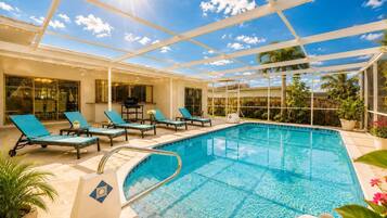 An indoor swimming pool with lounge chairs, a glass ceiling, and a view of the sky.