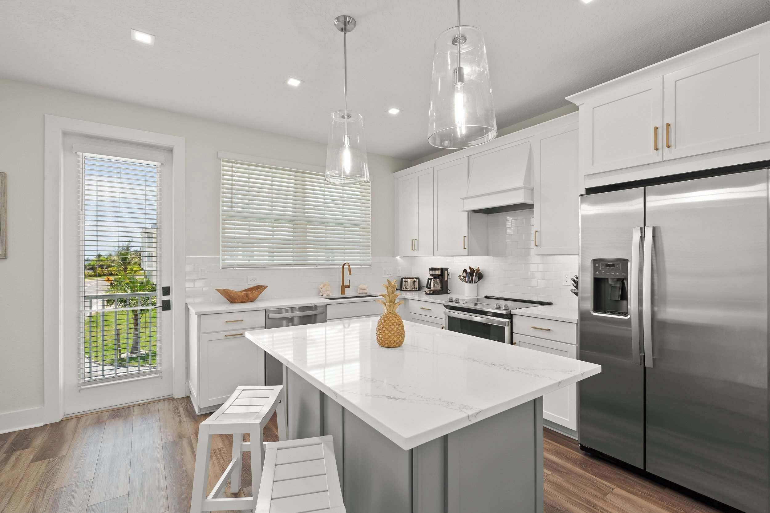 A modern kitchen with white cabinetry, a central island, stainless steel appliances, and pendant lighting.