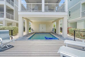 A rooftop pool with a wooden deck, lounge chairs, and a two-story building with balconies.