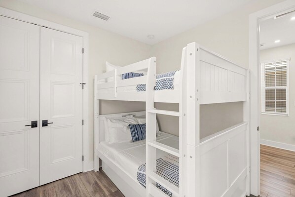 A bunk bed with patterned bedding, a white wardrobe, and a window with blinds.