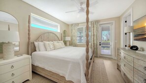 Een slaapkamer met een bed, nachtkastjes, een kaptafel, een plafondventilator en een raam met gordijnen.