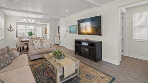 A living room with a sofa, coffee table, TV, fireplace, and a dining area in the background. - Luxury Home in Resort Community Private Pool Game & Room Baydream Believer at Hunters Point (Cortez)