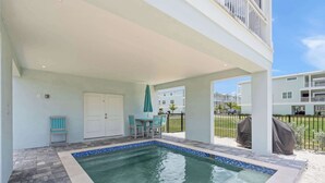 A covered outdoor swimming pool with a tiled edge, a table with chairs, and a door. - Luxury Home in Resort Community Private Pool Game & Room Baydream Believer at Hunters Point (Cortez)