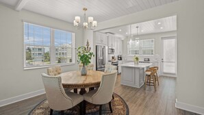 A modern kitchen with white cabinetry, a central island, and a dining area with a round table and chairs. - Luxury Home in Resort Community Private Pool Game & Room Baydream Believer at Hunters Point (Cortez)
