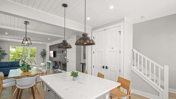 A modern kitchen with a marble island, pendant lighting, and a dining area with a blue sofa. - Luxury Waterfront Home in Resort Community Sea Salt at Hunters Point (Cortez)