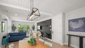 A modern dining area with a wooden table, white chairs, a blue sofa, and a kitchen with a dark wood backsplash. - Luxury Waterfront Home in Resort Community Sea Salt at Hunters Point (Cortez)