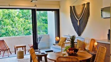 A modern dining area with a round table, wicker chairs, and a view of lush greenery outside.