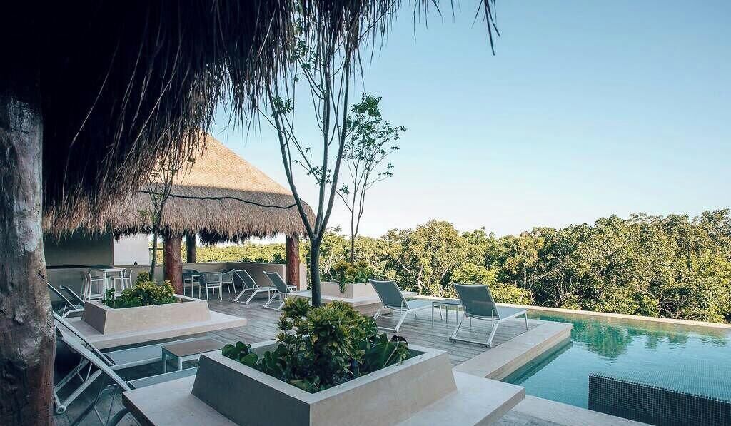 Un área de piscina al aire libre con sillones de descanso y una estructura de techo de paja.