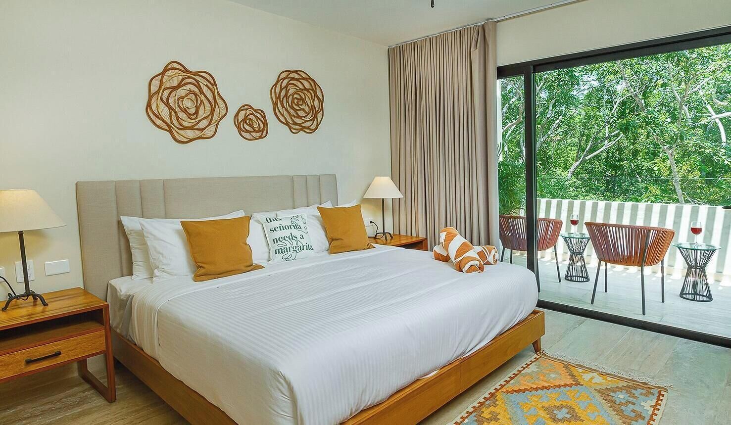 Habitación de hotel con una cama grande, dos mesitas de noche, una ventana con vistas a zonas verdes y un balcón con sillas.