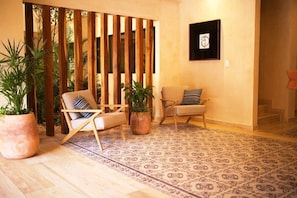 Una habitación con dos sillas, un tapete estampado, un separador de madera y plantas en macetas.