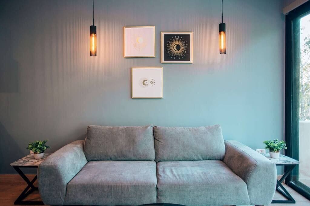 Una sala moderna con un sofá gris, dos lámparas colgantes y cuadros en la pared.