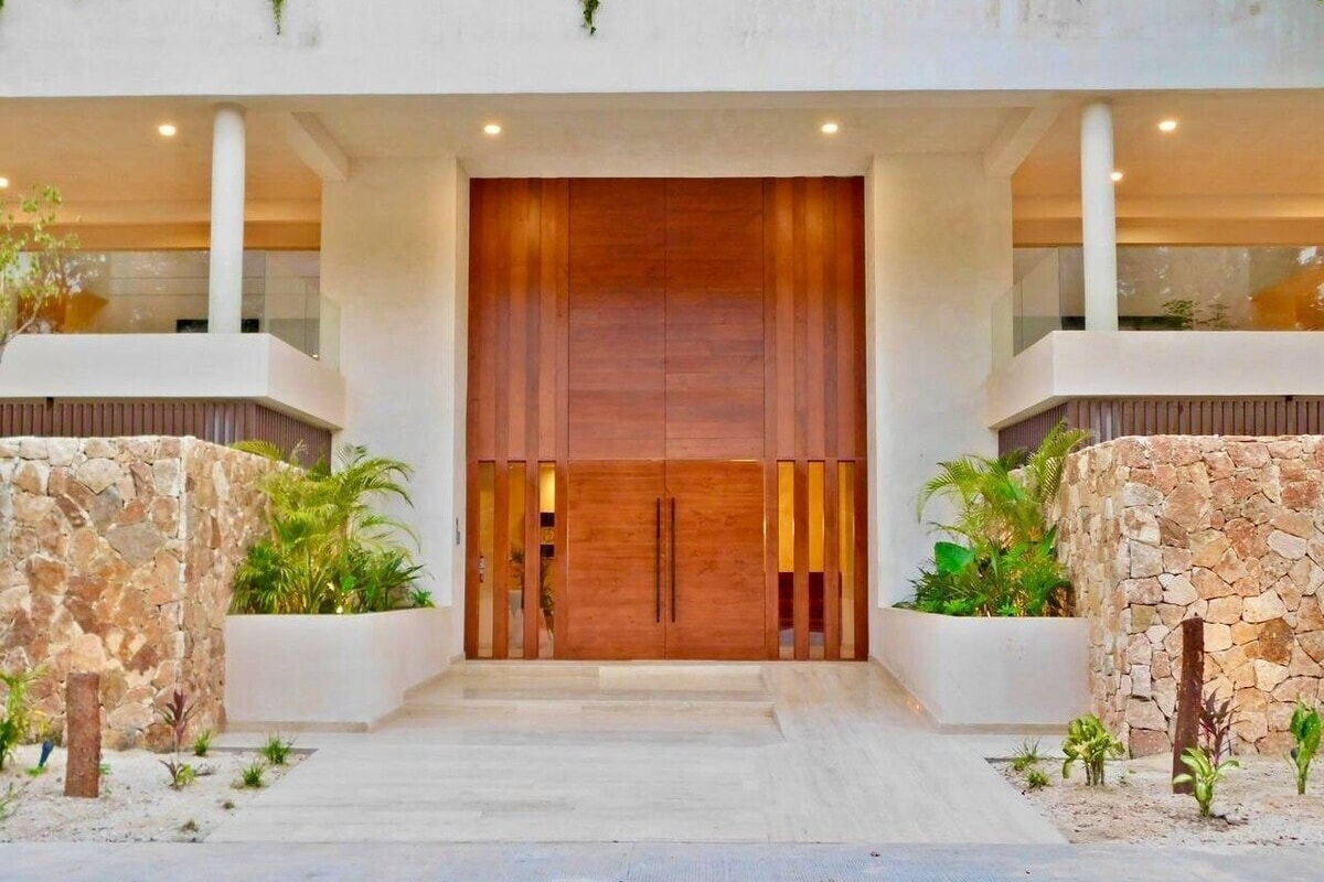 Una entrada de edificio moderna con una puerta de madera grande, paredes de piedra y plantas en macetas.