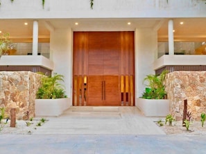 Una entrada de edificio moderna con una puerta de madera grande, paredes de piedra y plantas en macetas.