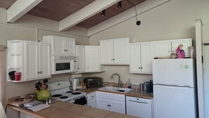 Una cocina con armarios blancos, microondas, estufa, lavaplatos y refrigerador.