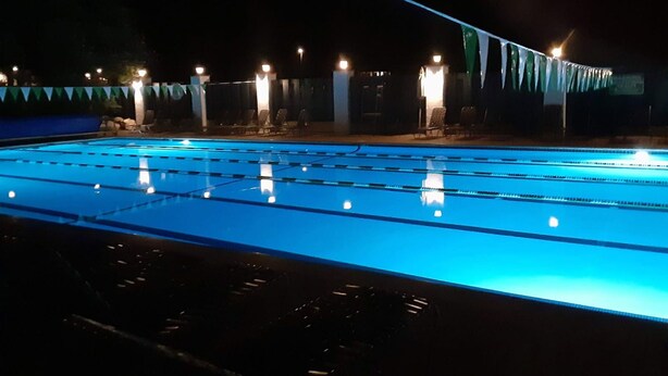 Una piscina con separadores de carril, rodeada de sillas de descanso y una zona cubierta con banderas.