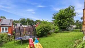 A grassy backyard with a trampoline, a slide, and a play structure.