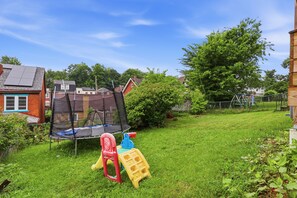 A grassy backyard with a trampoline, a slide, and a play structure.