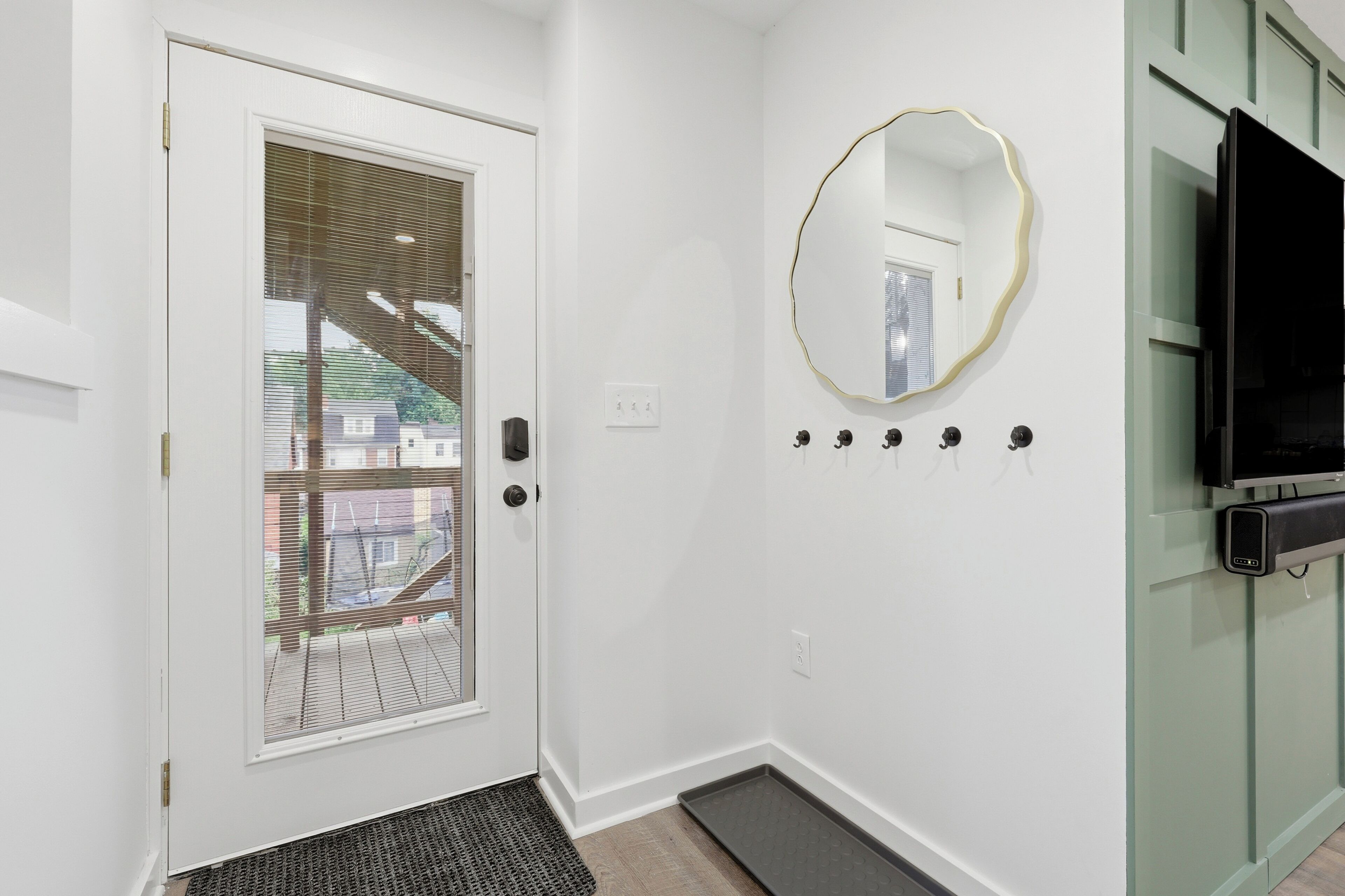 Un couloir avec une porte blanche, un petit miroir, un téléviseur à écran plat et un trousseau de clés accroché au mur.