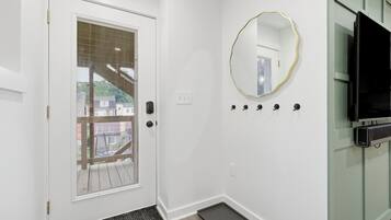 Un couloir avec une porte blanche, un petit miroir, un téléviseur à écran plat et un trousseau de clés accroché au mur.